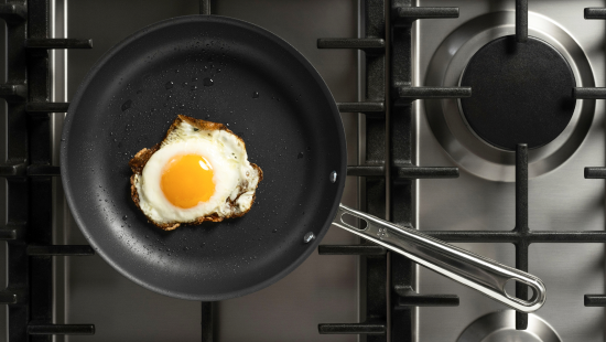 Fried egg in a black nonstick frying pan on a stainless steel gas stovetop, handle extending right.