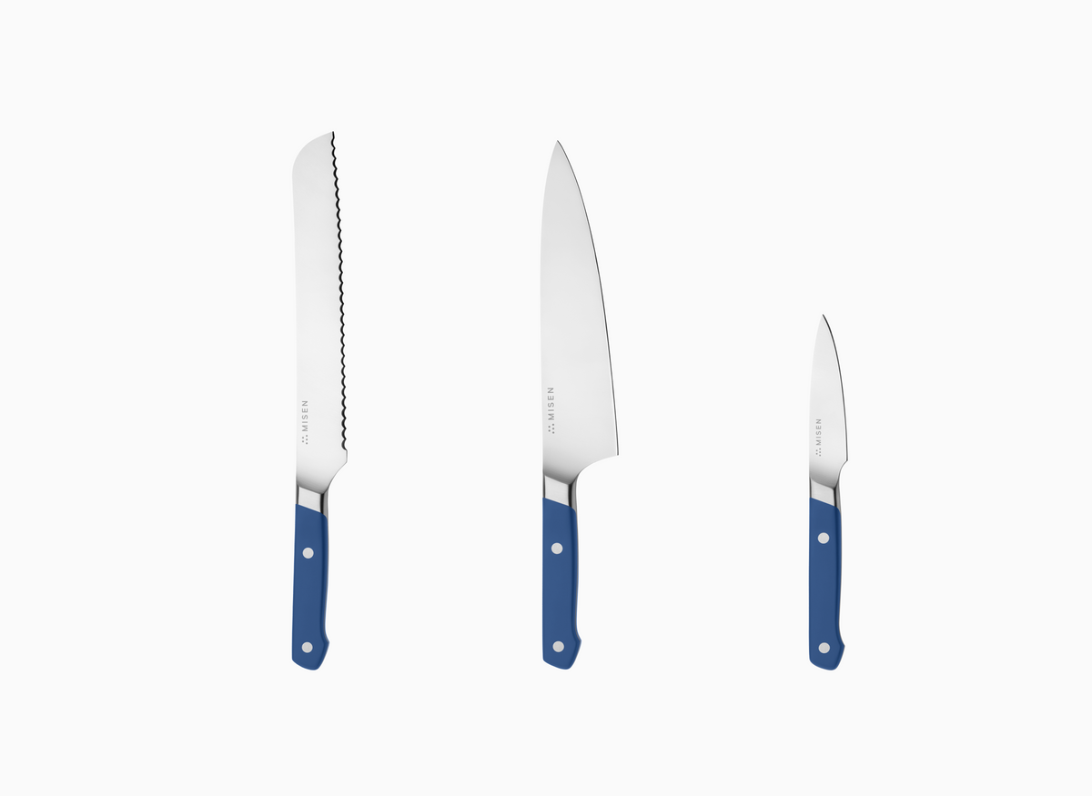 The image displays a set of three Misen knives with blue handles and AUS-10 steel blades, arranged vertically against a white background. From left to right, the knives decrease in size. The leftmost knife is the longest and features an 8 inch serrated blade. The middle knife has a smooth, curved blade and is an 8 inch chef's knife. The rightmost knife is the smallest, with a straight, smooth blade, resembling a paring knife. Each knife has the word "MISEN" faintly visible near the handle on the blade.