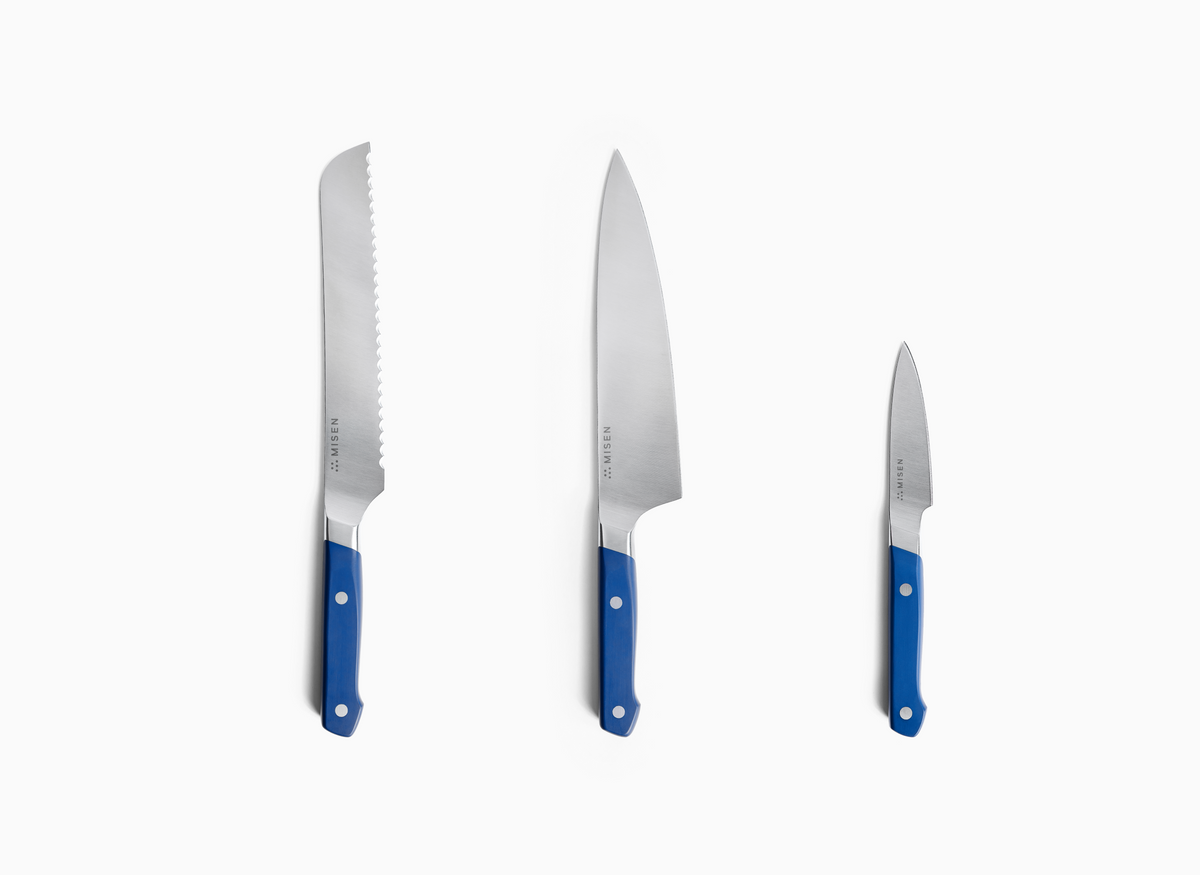 Three blue-handled knives are shown upright against a white background. From left to right, there is an 8 inch Serrated Knife 2.0, an 8n inch Chef's Knife 2.0, and a 3.5 inch Paring Knife 2.0. Each knife has a silver-toned ACUTO440 steel blade with "MISEN" and a logo engraved on it. The handles are a vibrant blue with visible rivets.