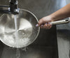 A hand holds a Misen Stainless Steel Pan under running water in a kitchen sink. 