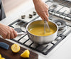 A hand uses a whisk to whip lemon curd in a Misen Stainless Steel Saucier on a stovetop.