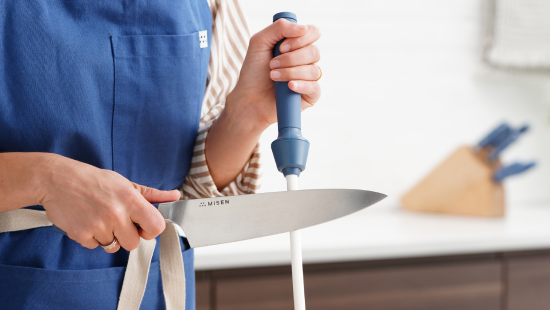 Person in blue apron using honing rod to sharpen Misen chef's knife