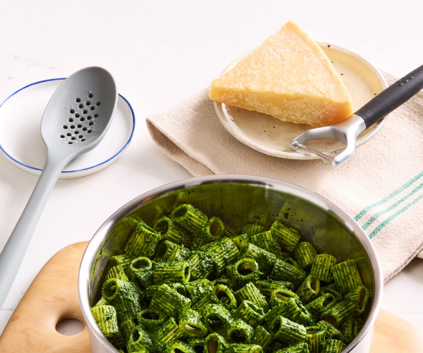 Rigatoni pasta with vibrant green pesto sauce in stainless steel pan with Parmesan cheese