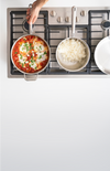 Overhead gas range with skillet of tomato-and-egg dish with herbs, saucepan of rice, hand holding skillet handle