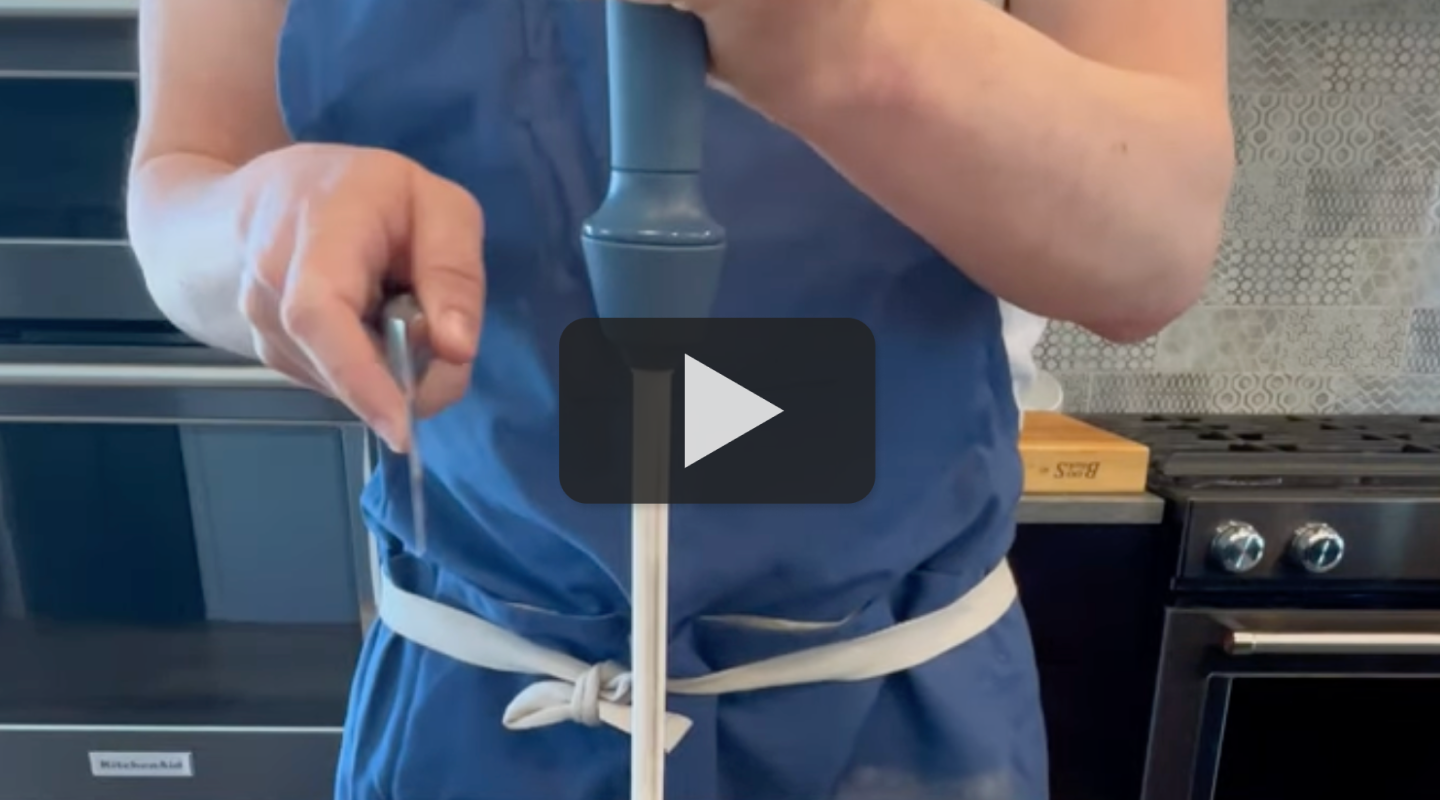 Person in blue apron using immersion blender in modern kitchen