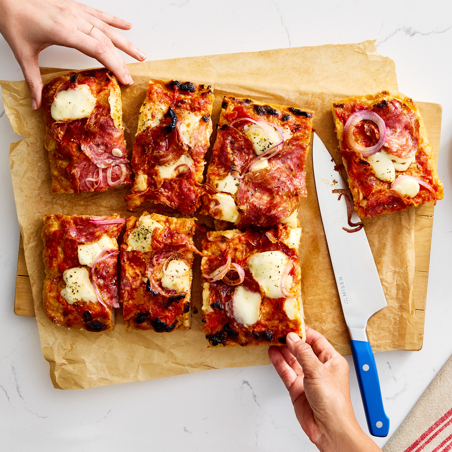 Homemade sheet pan pizza with salami, mozzarella, and red onion cut into squares
