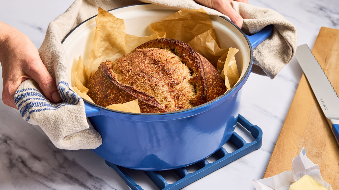 Freshly baked sourdough bread in a blue enameled Dutch oven on a trivet
