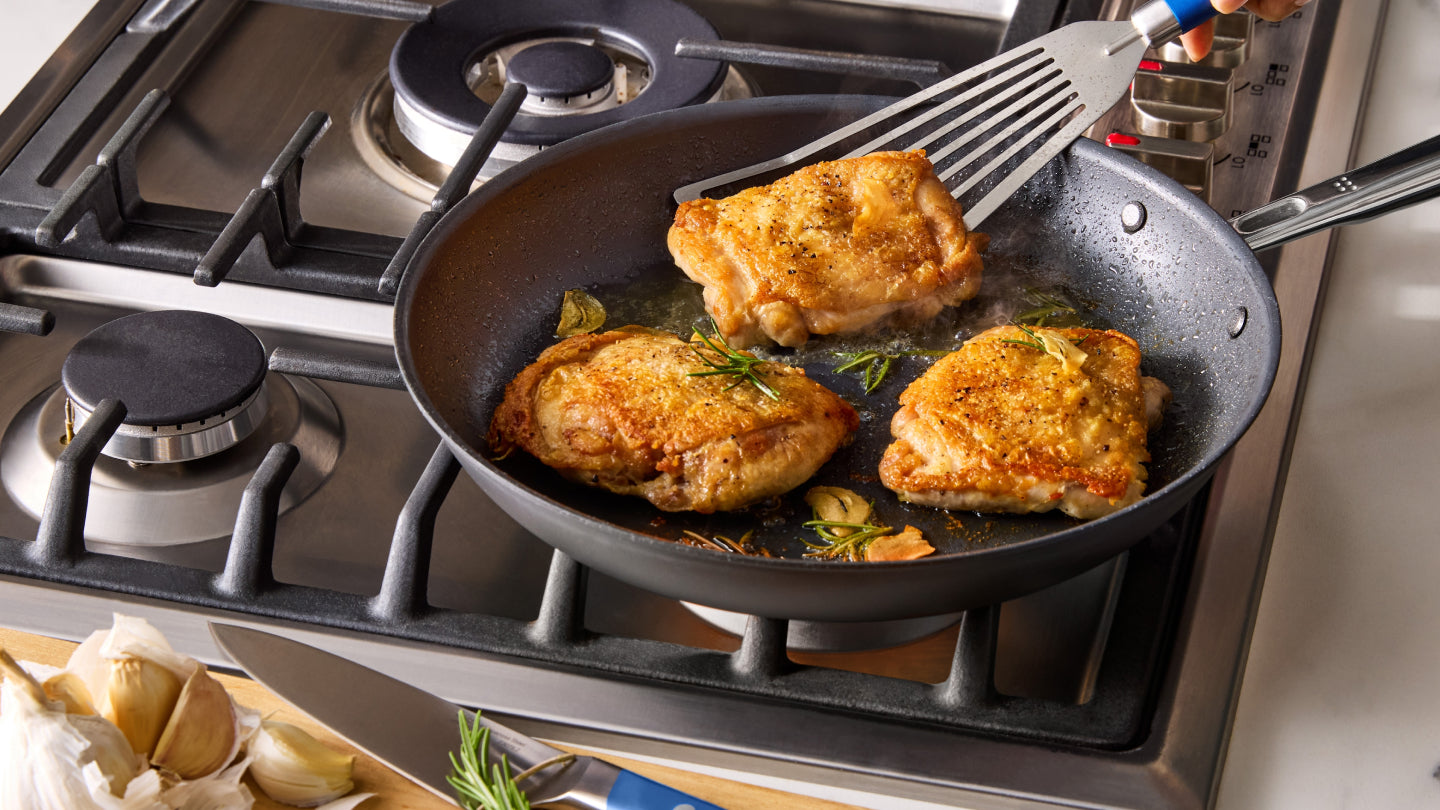 Golden brown chicken thighs pan-searing in nonstick skillet with rosemary and garlic on gas stove