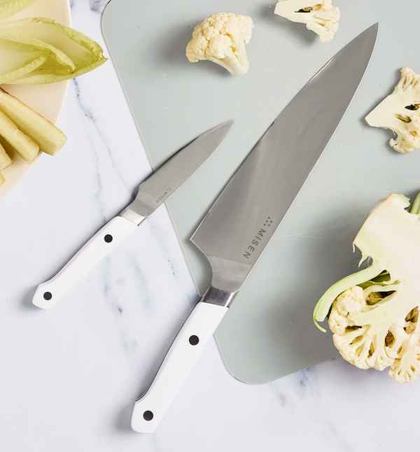 Misen chef's knife and paring knife with white handles on cutting board with cauliflower