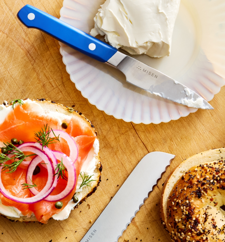 Misen knife spreading cream cheese on everything bagel with smoked salmon, capers, and red onion
