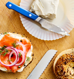 Misen knife spreading cream cheese on everything bagel with smoked salmon, capers, and red onion