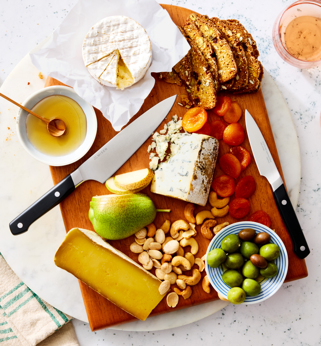 Cheese board with brie, blue cheese, aged cheese, pear, cashews, olives, dried apricots, and seeded crackers