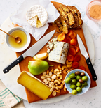 Cheese board with brie, blue cheese, aged cheese, pear, cashews, olives, dried apricots, and seeded crackers