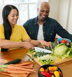 Couple smiling while chopping fresh vegetables together in kitchen