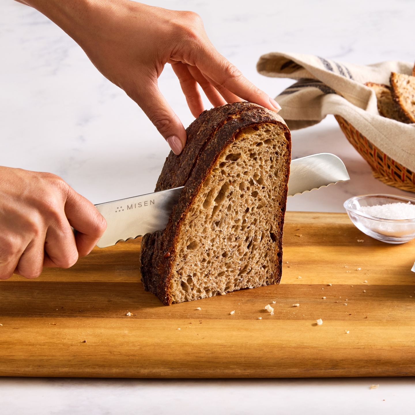Misen bread knife slicing dark sourdough loaf on wooden cutting board