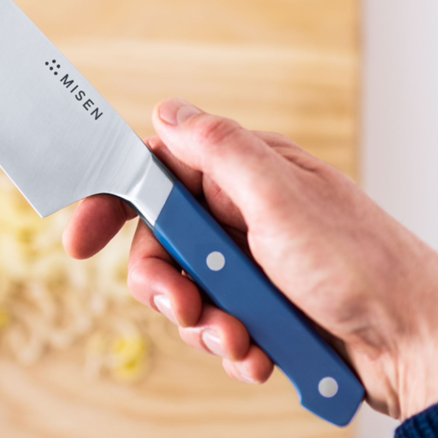 Misen chef's knife with blue G10 handle held in pinch grip