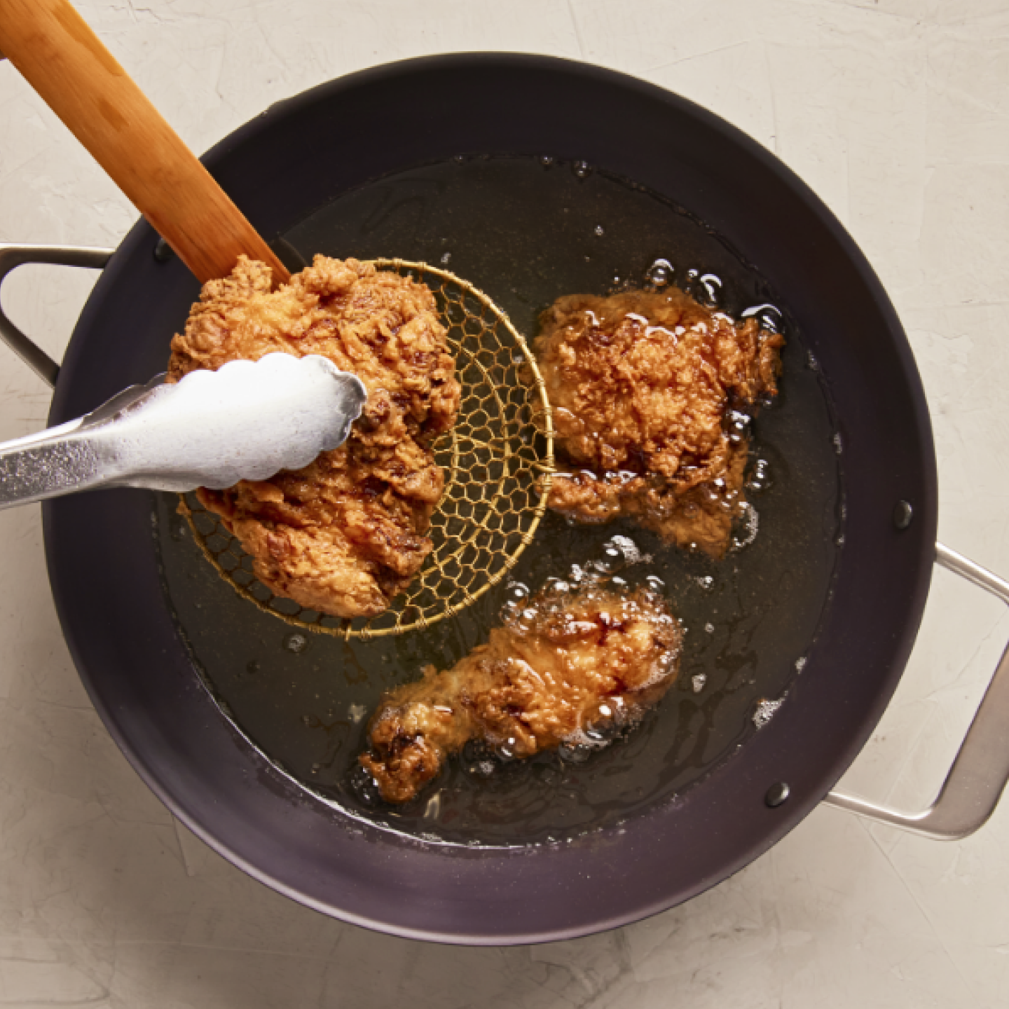 Golden crispy fried chicken pieces being lifted from hot oil in a deep pan with a wire skimmer
