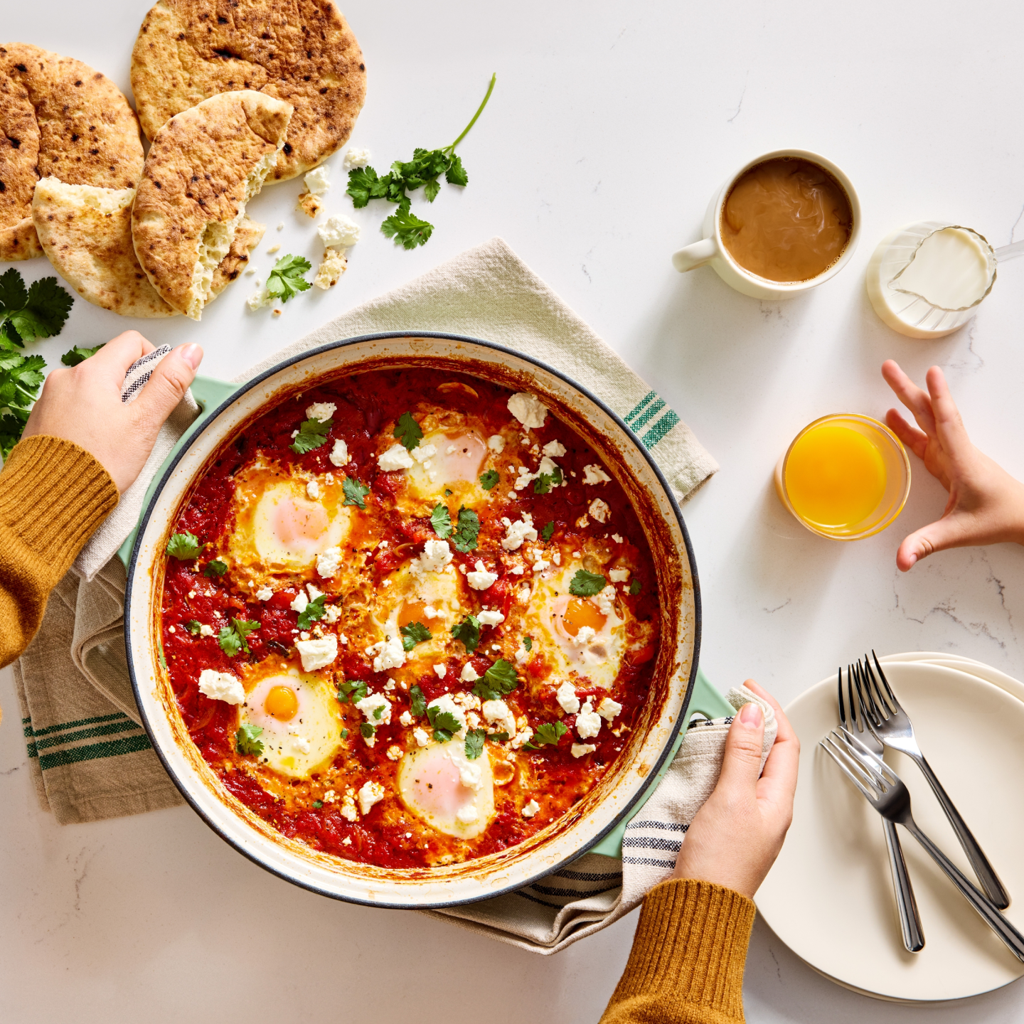 Shakshuka with poached eggs, feta, and cilantro served in a skillet with pita bread