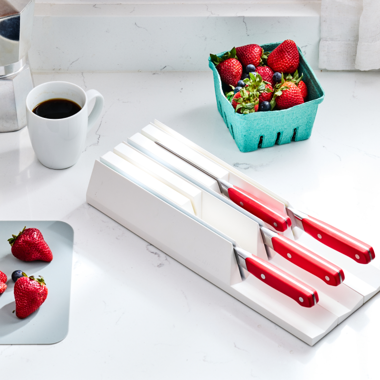 Red-handled kitchen knives in white countertop knife block with fresh strawberries and coffee