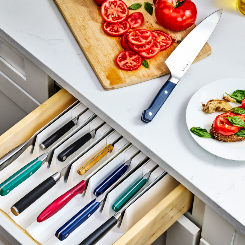 Colorful kitchen knives organized in drawer insert beside sliced tomatoes on cutting board