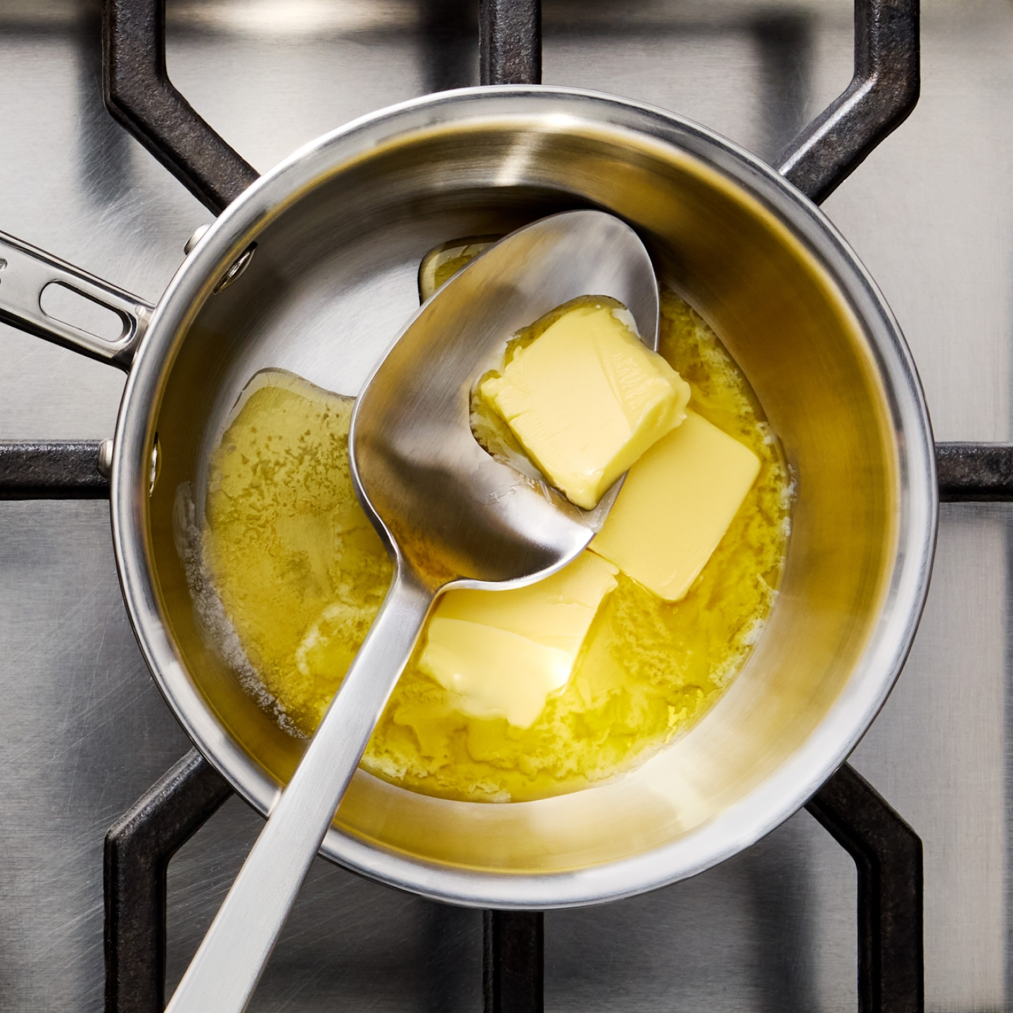 Butter melting in stainless steel saucepan on gas stove with spoon