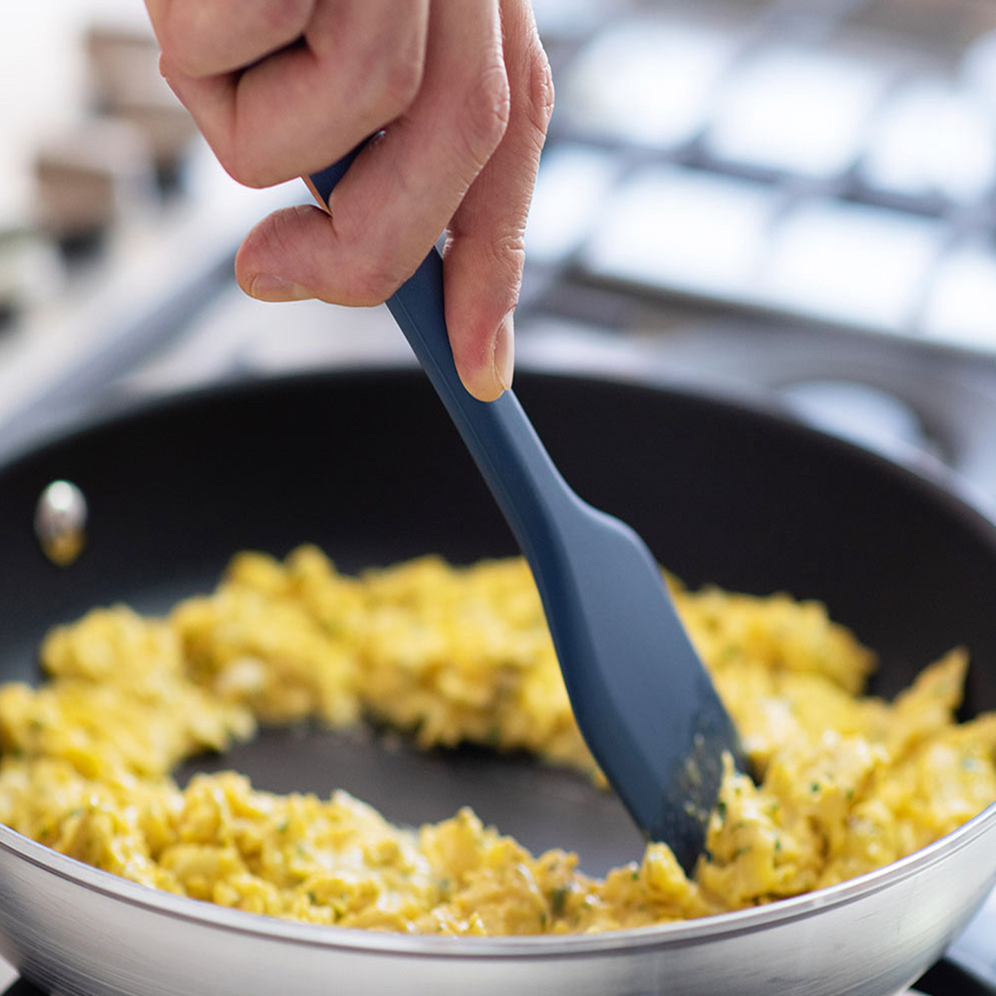 Scrambled eggs being stirred in a nonstick pan with a blue silicone spatula