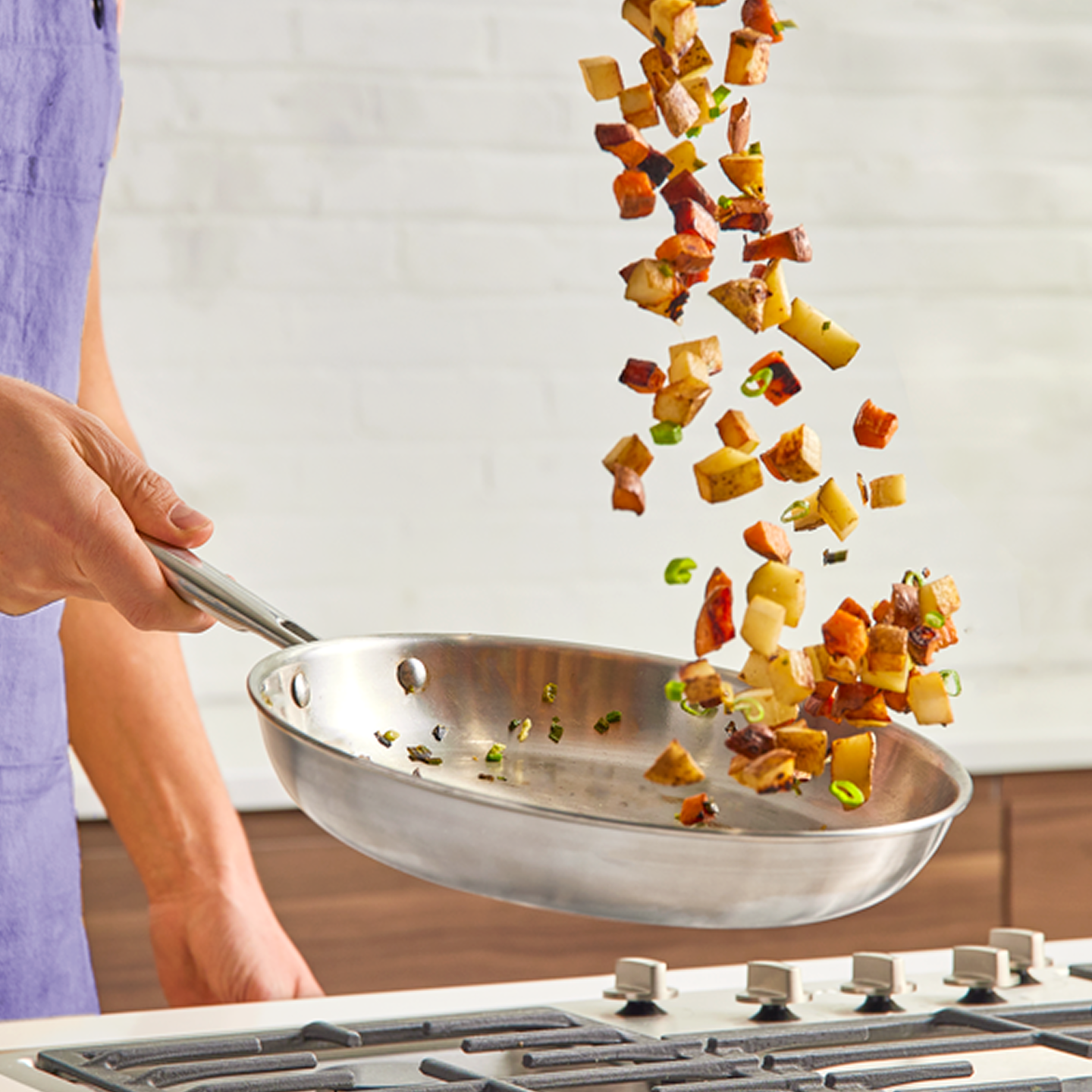 Chef tossing sautéed potato hash in stainless steel skillet on gas stove