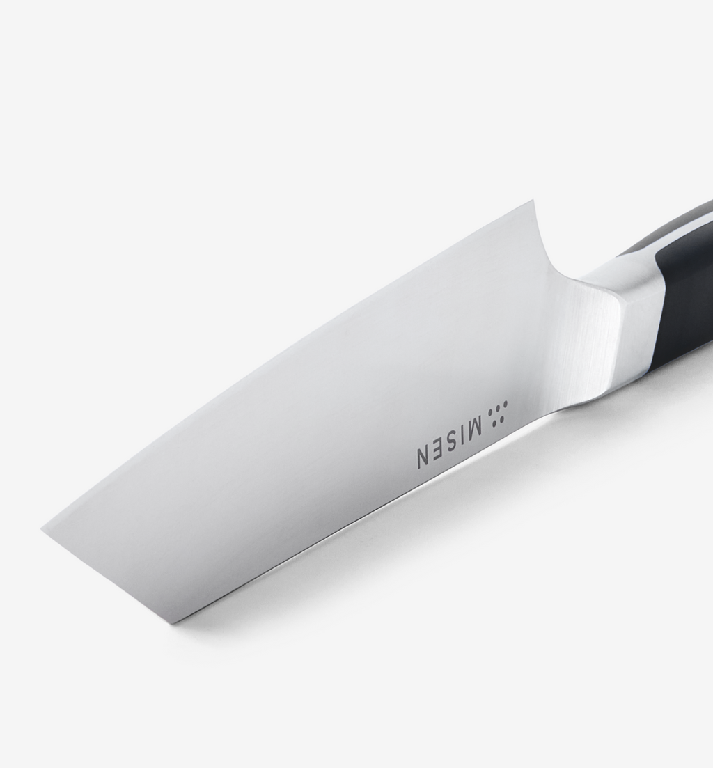 Misen chef's knife blade close-up showing polished stainless steel and bolster