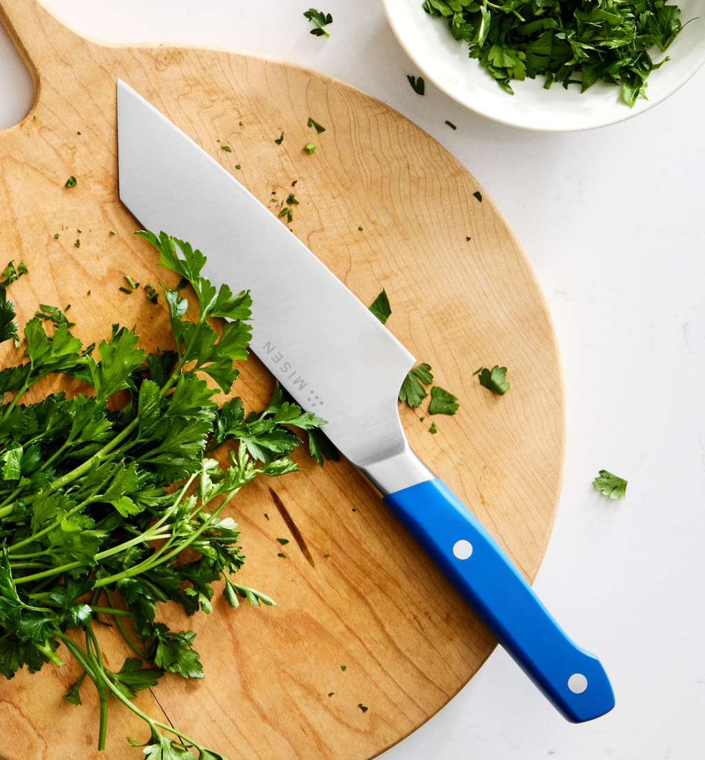 Misen chef's knife with blue handle on wooden cutting board with fresh parsley