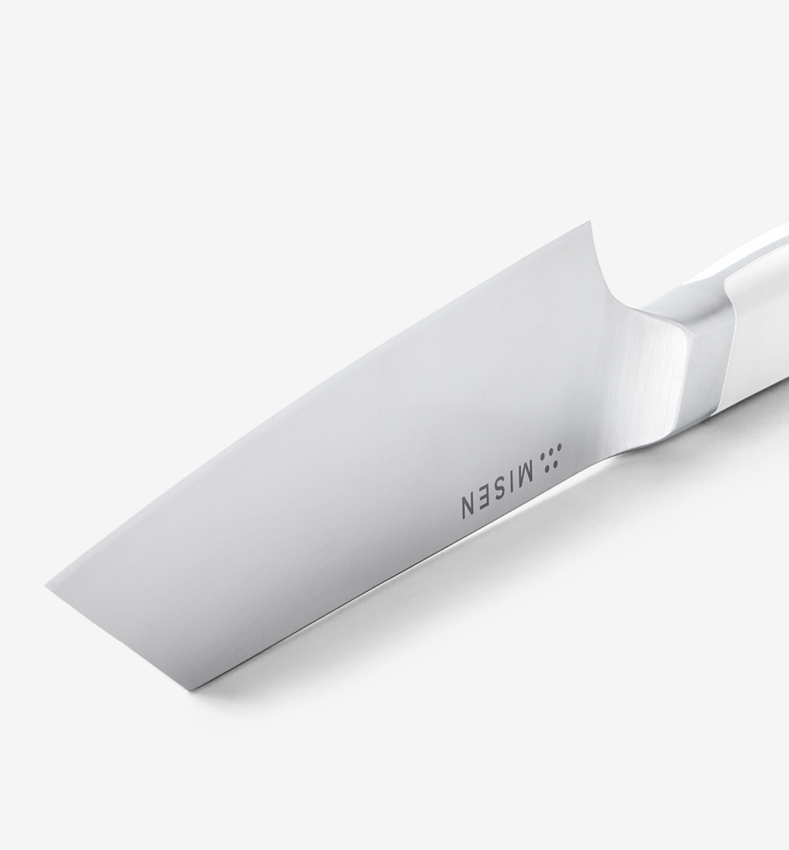 Misen chef's knife blade close-up showing polished stainless steel and bolster