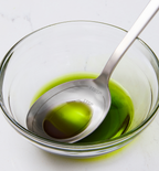 Bright green liquid in glass bowl with stainless steel measuring spoon showing 1 tablespoon and 1 teaspoon markings