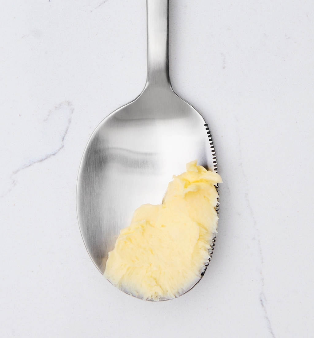 Softened butter on a stainless steel spoon against marble surface