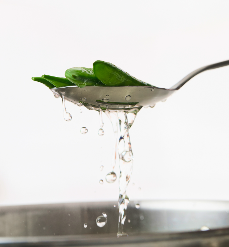Fresh snap peas lifted from boiling water on a slotted spoon while blanching
