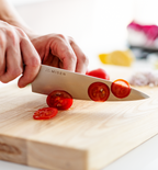 Misen chef's knife slicing cherry tomatoes on a wooden cutting board