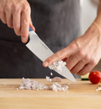 Chef dicing shallots with a Misen chef's knife on a wooden cutting board