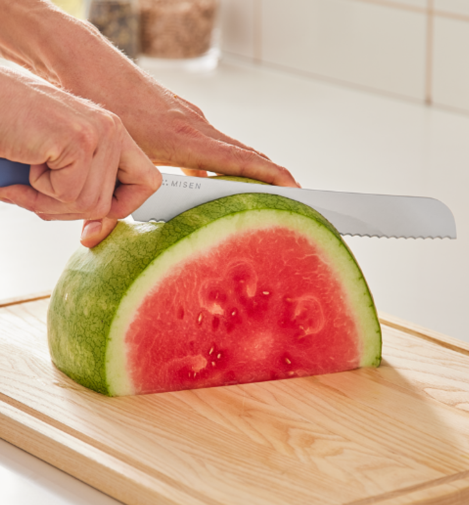 Misen serrated knife slicing a halved watermelon on a wooden cutting board