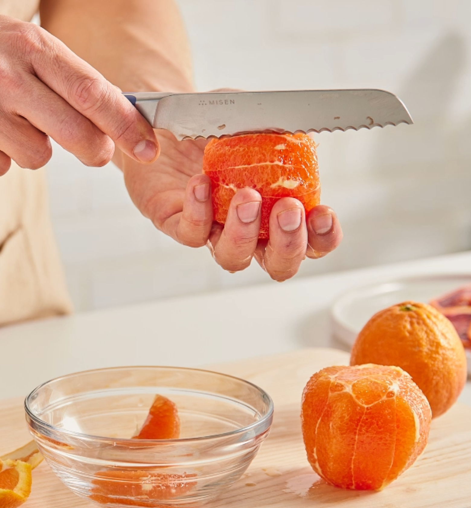 Misen serrated knife cutting peel from fresh orange over glass bowl