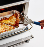 Spatula lifting reheated cheese pizza slice from toaster oven tray