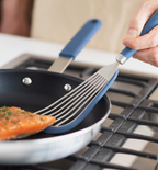 Fish spatula flipping seasoned salmon fillet in blue nonstick skillet on gas stovetop