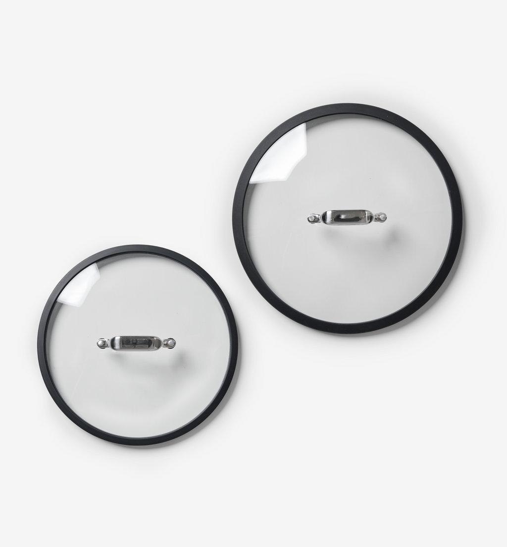Two glass pot lids with stainless steel handles and black silicone rims, different sizes