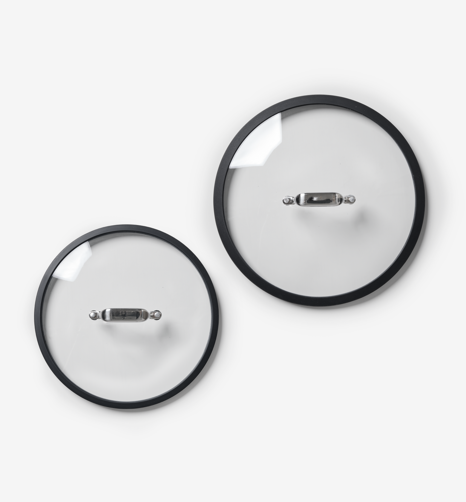 Two glass pot lids with stainless steel handles and black silicone rims, different sizes