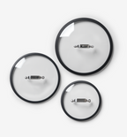 Set of three glass cookware lids with black rims and stainless steel handles in small, medium, and large sizes