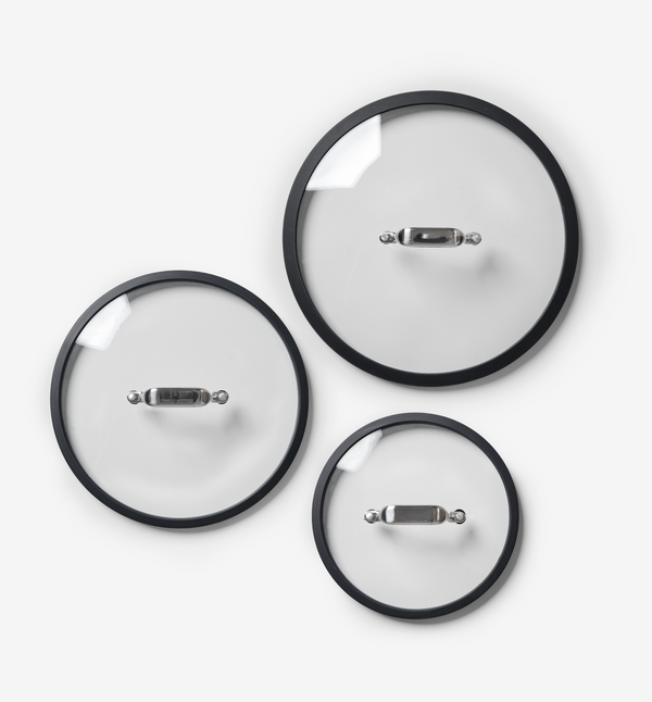 Set of three glass cookware lids with black rims and stainless steel handles in small, medium, and large sizes