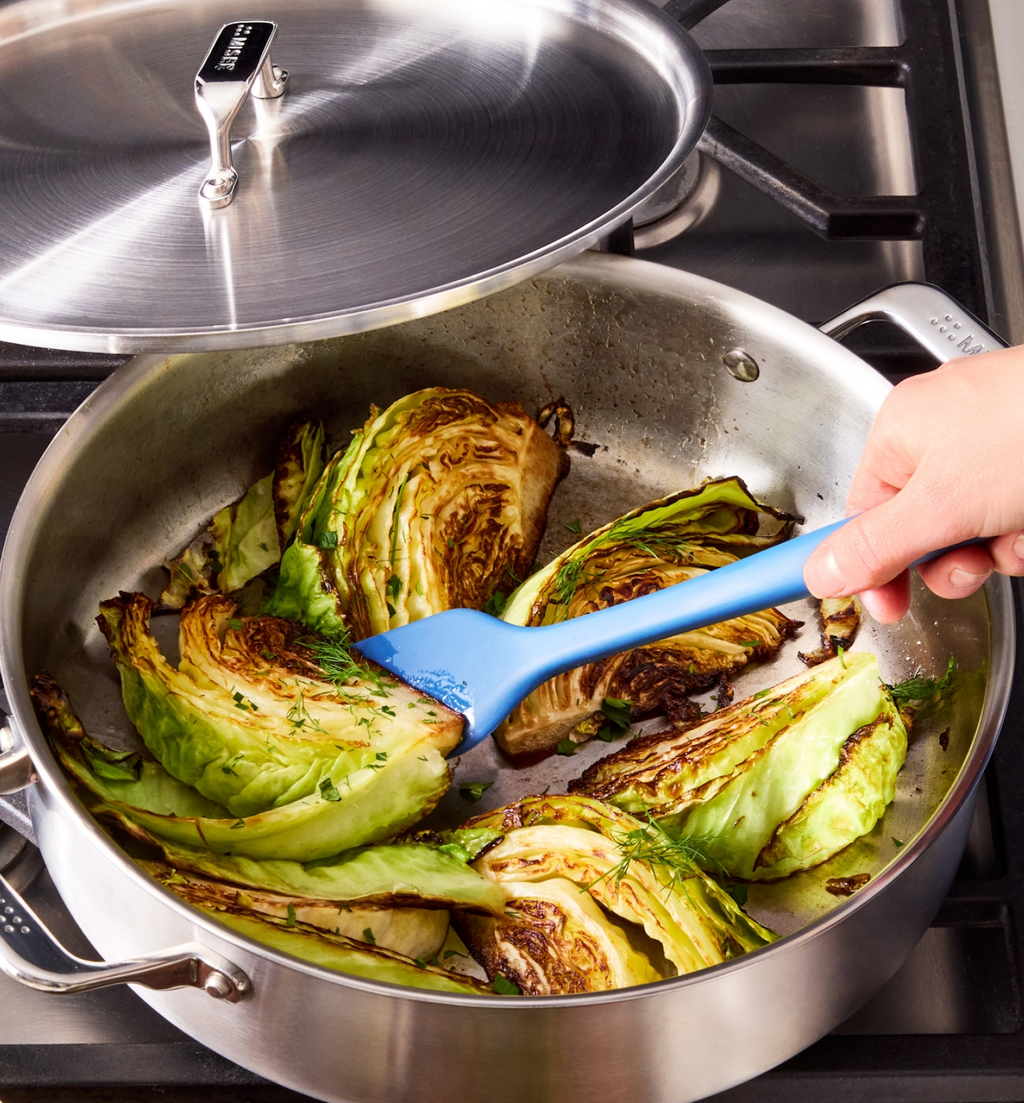 Sautéed cabbage wedges with fresh herbs in stainless steel pan on gas stove