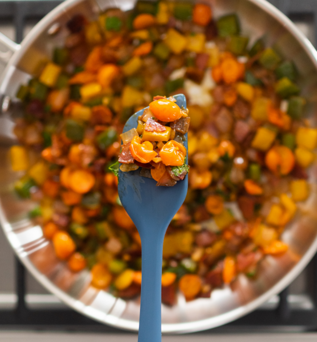 Sautéed vegetables with carrots, peppers, and bacon in a stainless steel pan