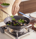 Chef adding fresh parsley to steamed mussels in a wok on a portable gas burner