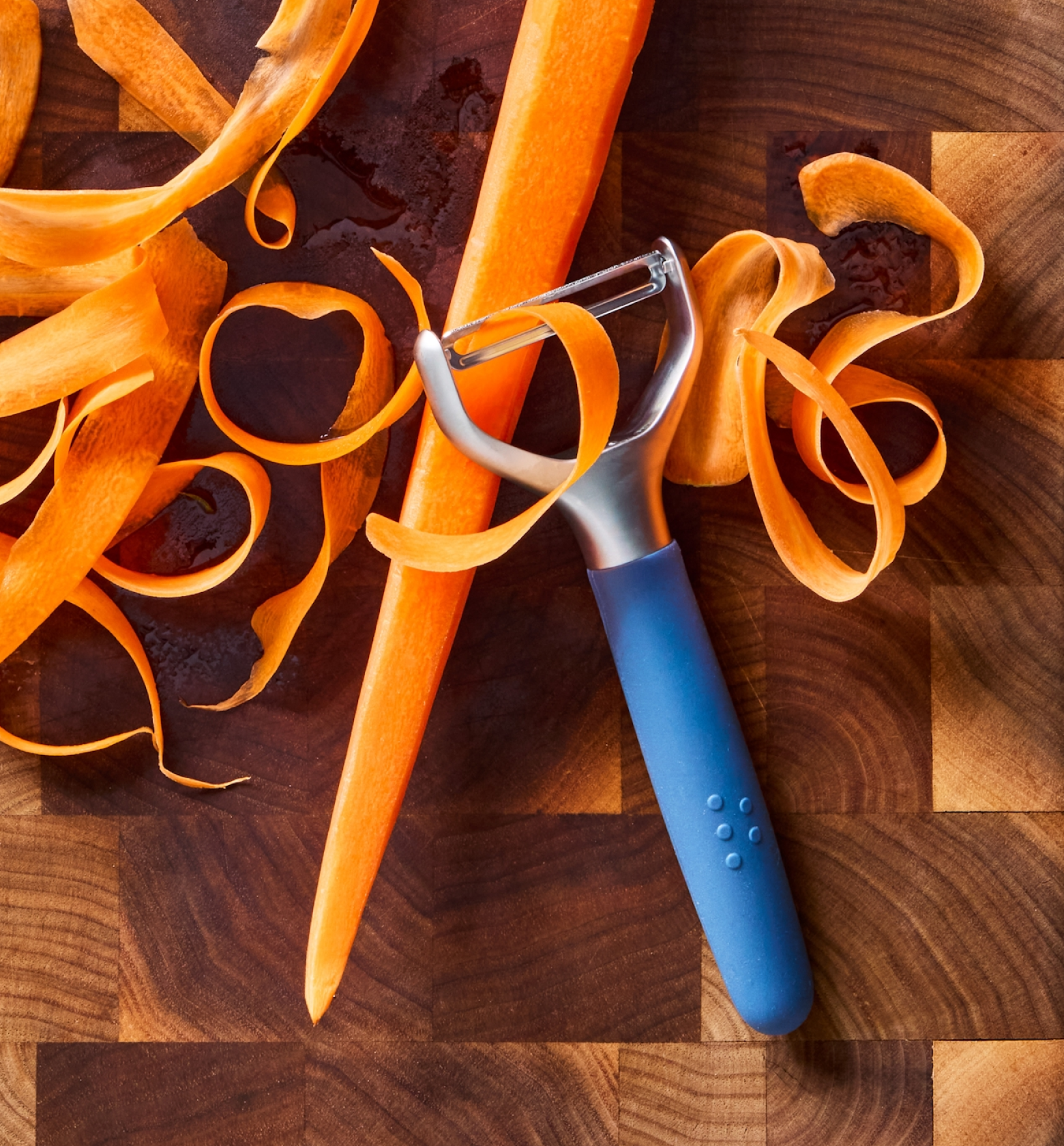 Y-peeler with blue handle peeling a carrot on a wooden cutting board