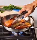 Pan-seared salmon fillets cooking in stainless steel skillet on gas stove