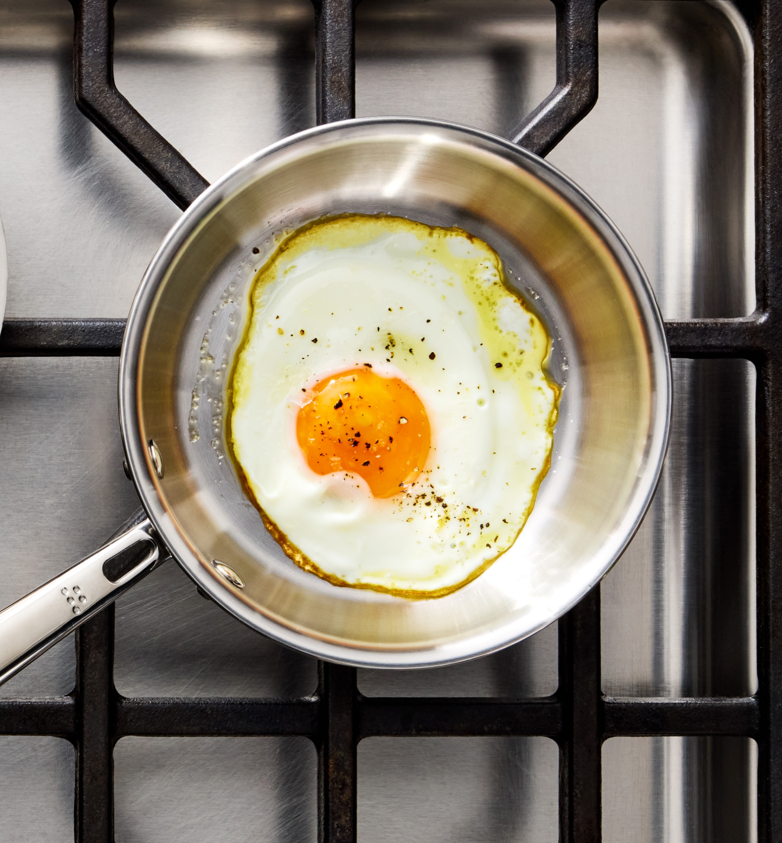 Sunny side up fried egg with black pepper in stainless steel pan on gas stove