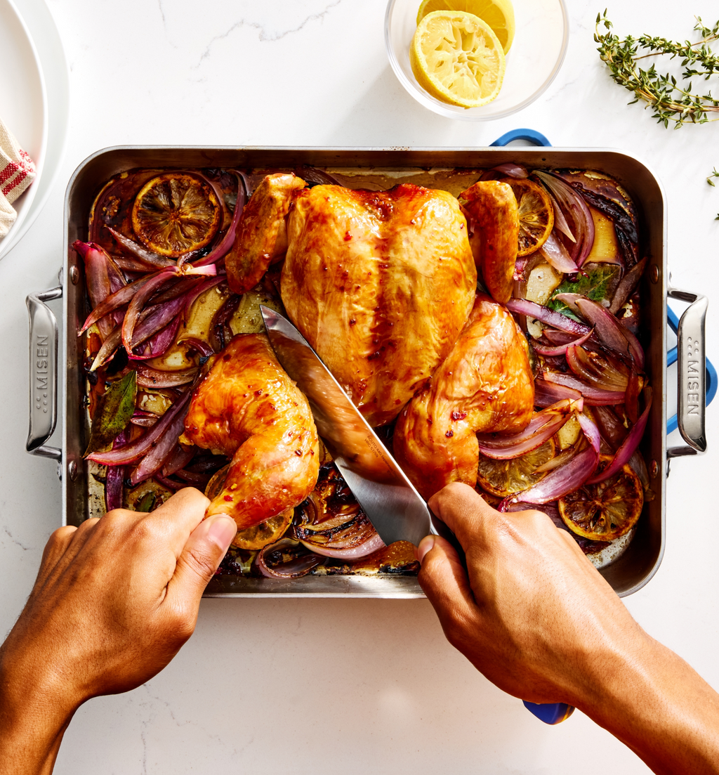 Carving a golden roasted whole chicken with lemon and red onion in a Misen roasting pan